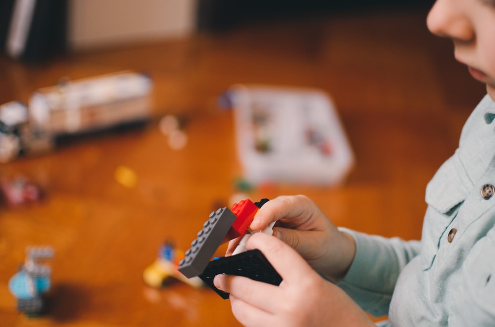 Close up of a child playing with legos, with more toys scattered in the background.